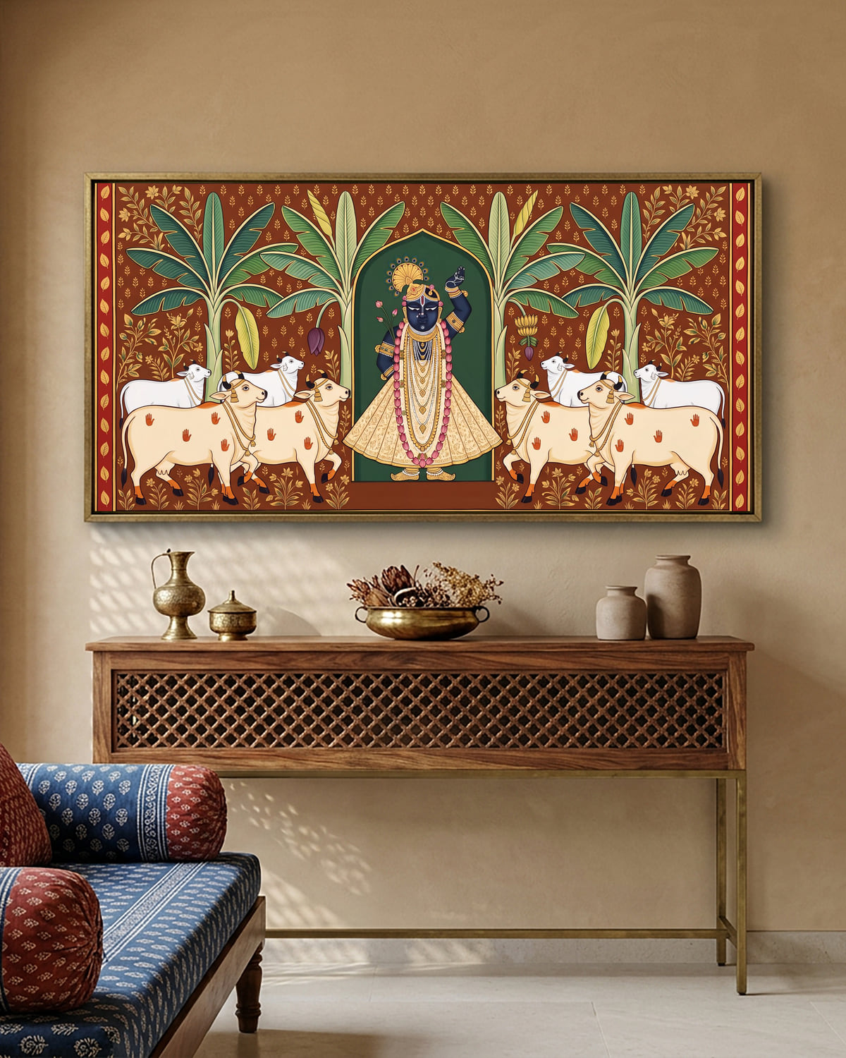 A wide Pichwai canvas of Gau Mata among banana leaves, above a console set with brass lamps